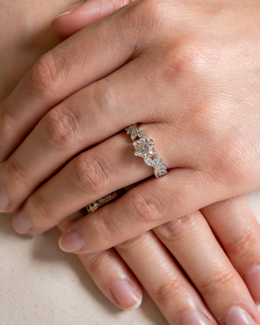 Silver ring with a round diamond center stone and leaf-shaped diamond accents on a hand.