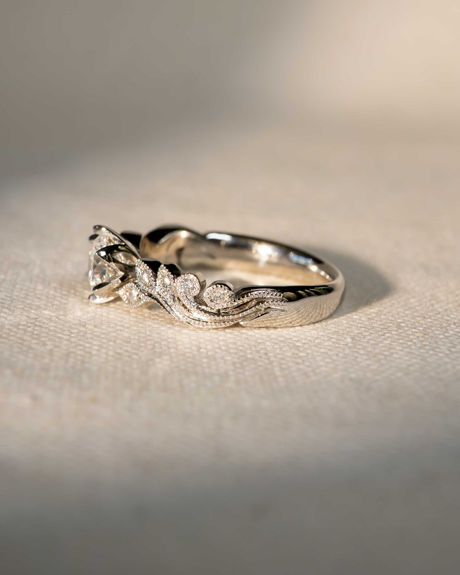 White gold ring with a round diamond center stone and beaded, leafy accents.