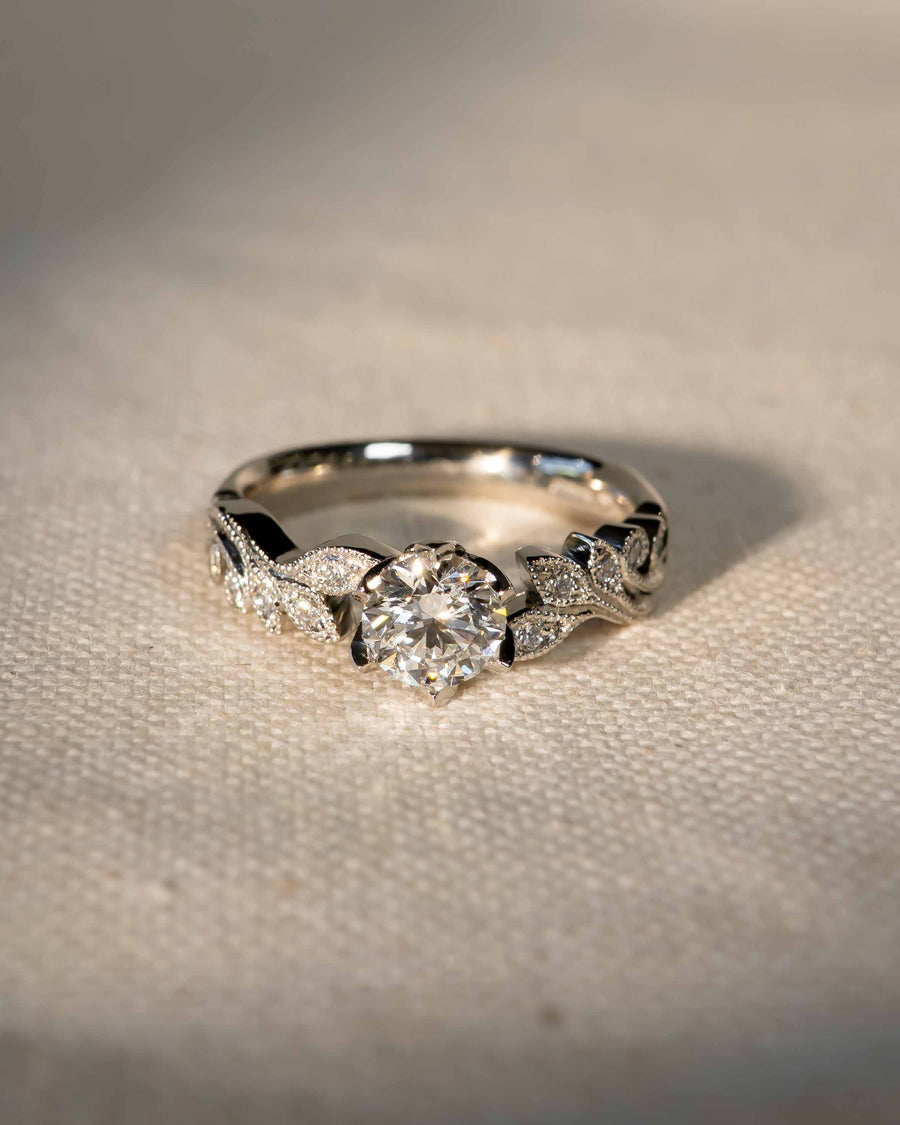 Platinum engagement ring with a round diamond and beaded leaf design.