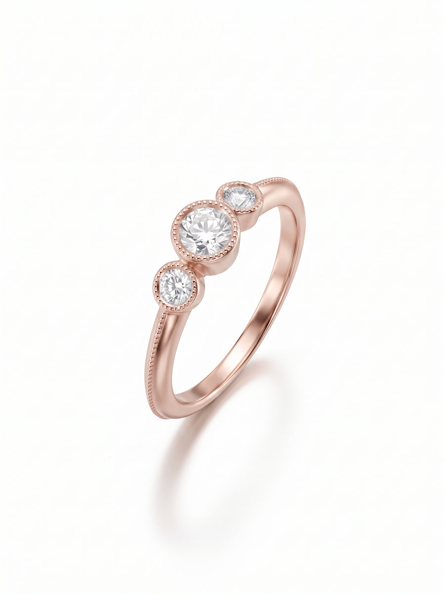 Rose gold trilogy engagement ring with three round diamonds in milgrain bezel settings.