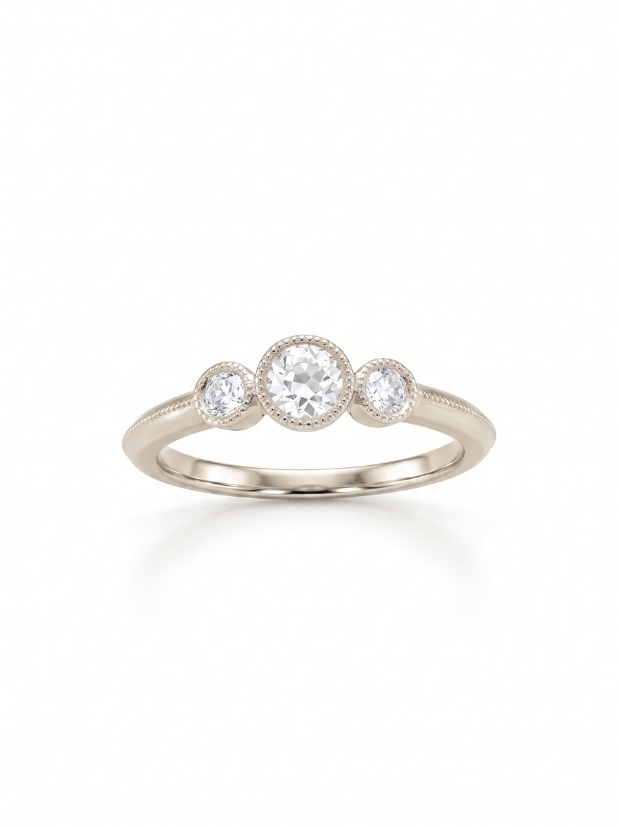 Vintage trilogy engagement ring in white gold with three round diamonds in milgrain bezel settings.