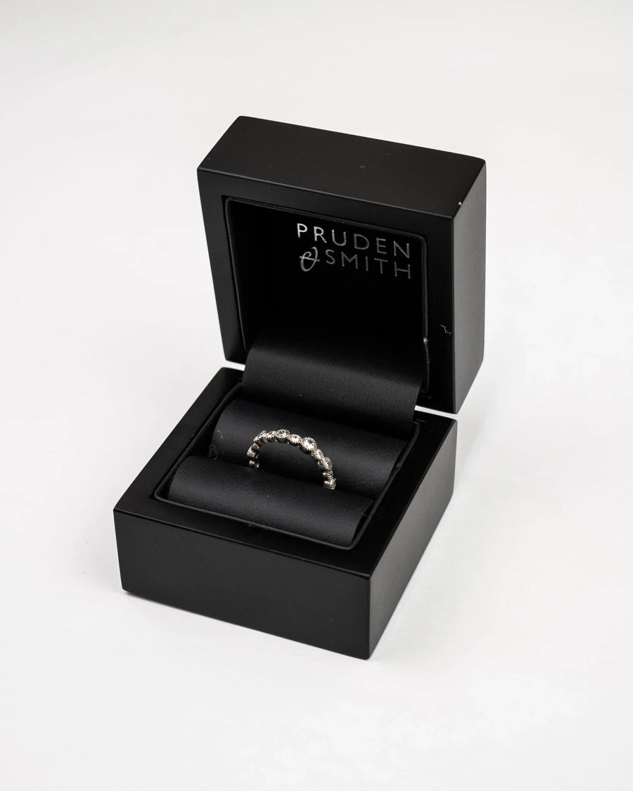 Silver eternity ring with small diamonds in an open black gift box.