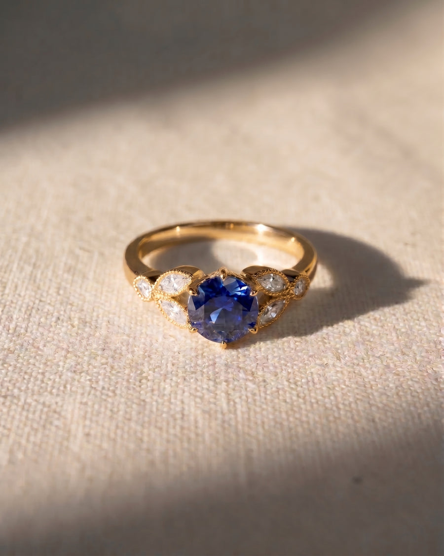 18ct rose gold ring with a round sapphire center stone and pear-shaped side diamonds.