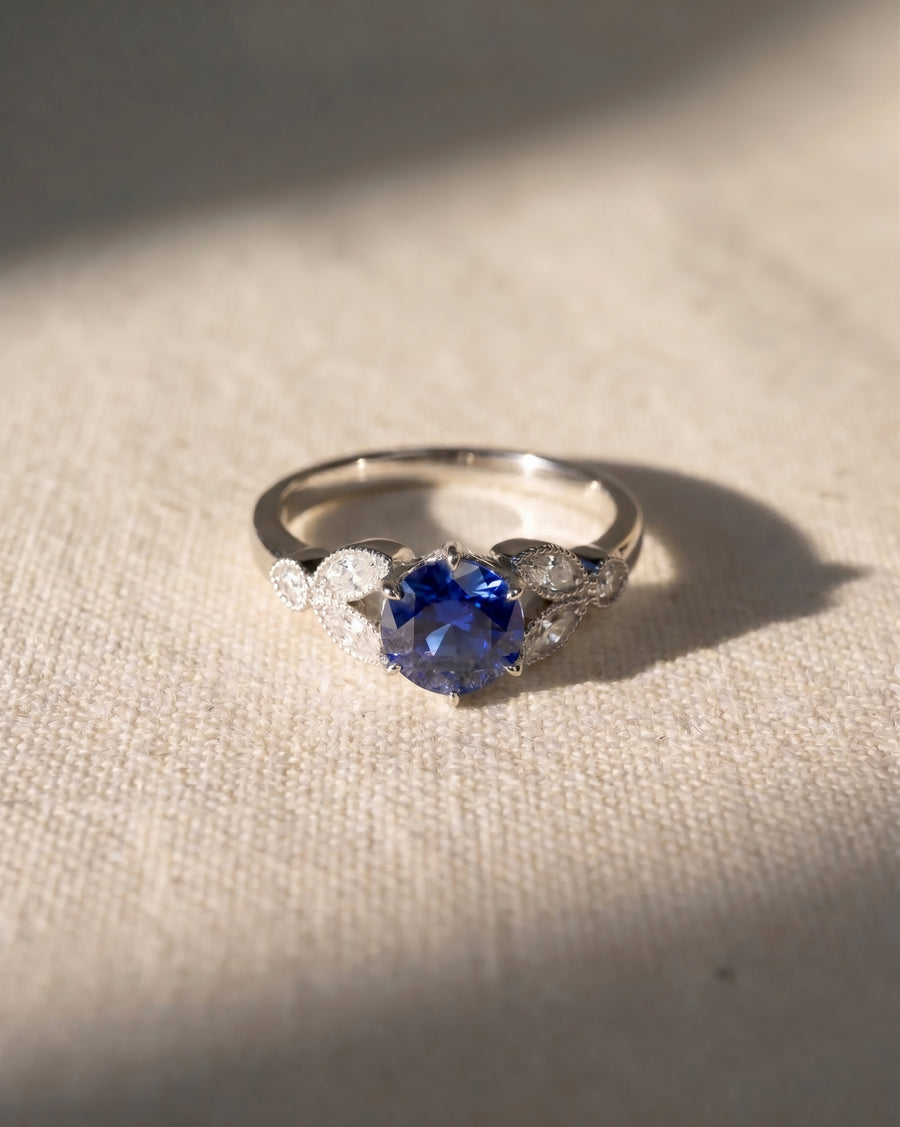 Platinum engagement ring with a round sapphire and marquise diamond accents.