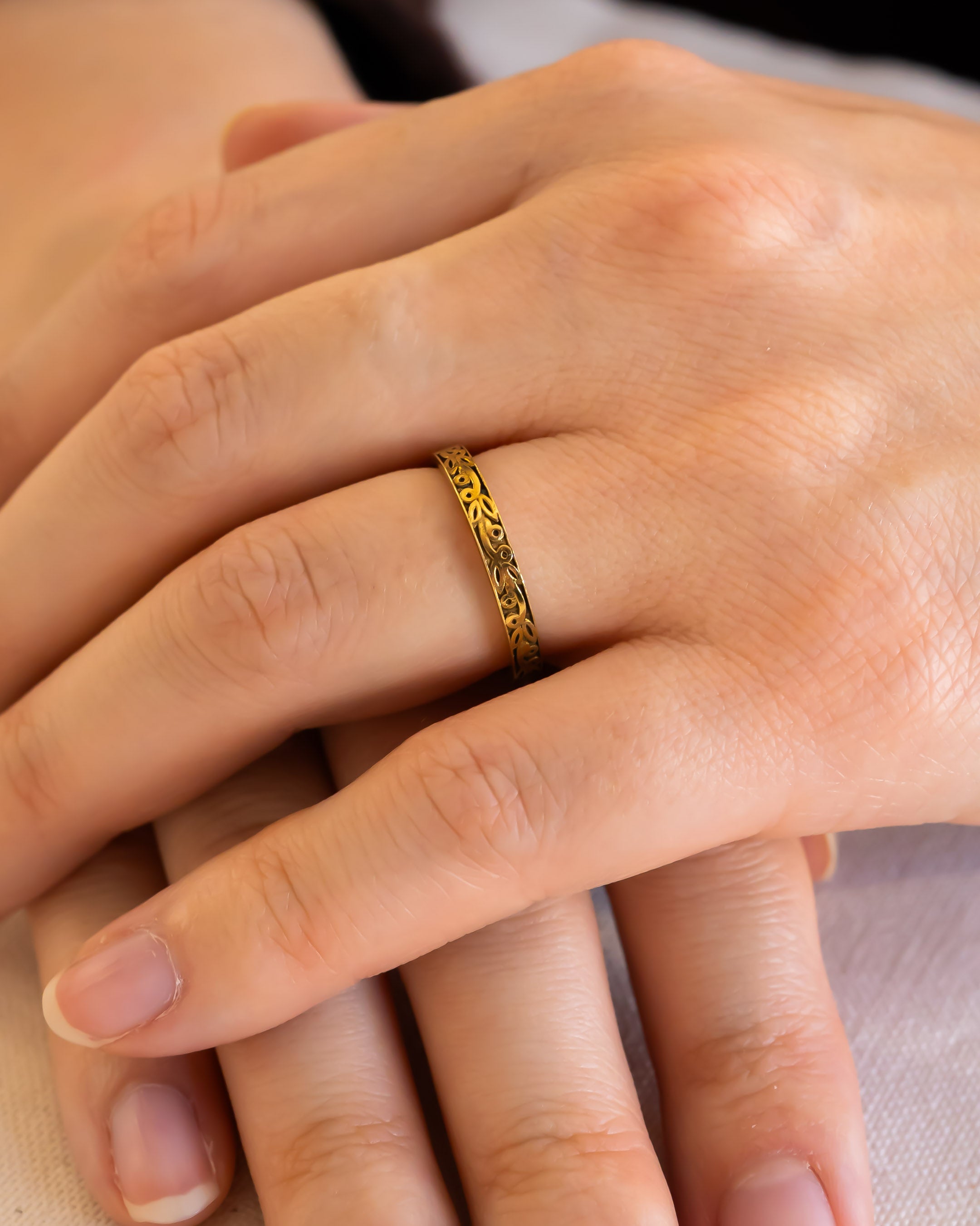 Hand wearing a delicate gold wedding ring with intricate engraved pattern
