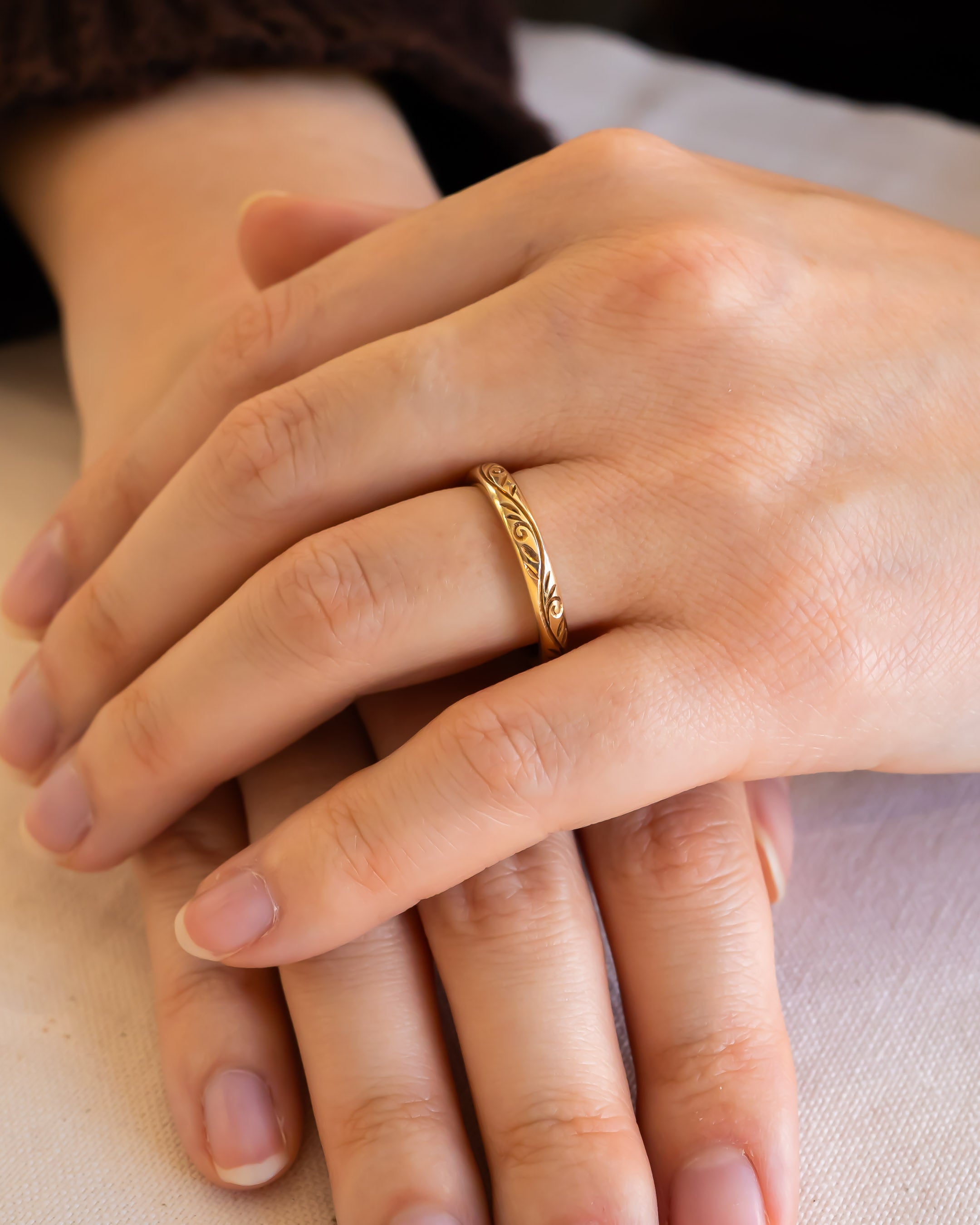 Hand wearing a gold wedding ring with engraved organic pattern, resting on another hand