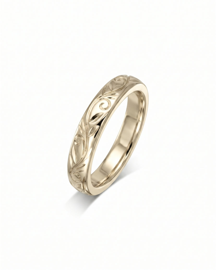 Gold wedding band featuring an engraved floral scroll pattern on a polished metal surface.