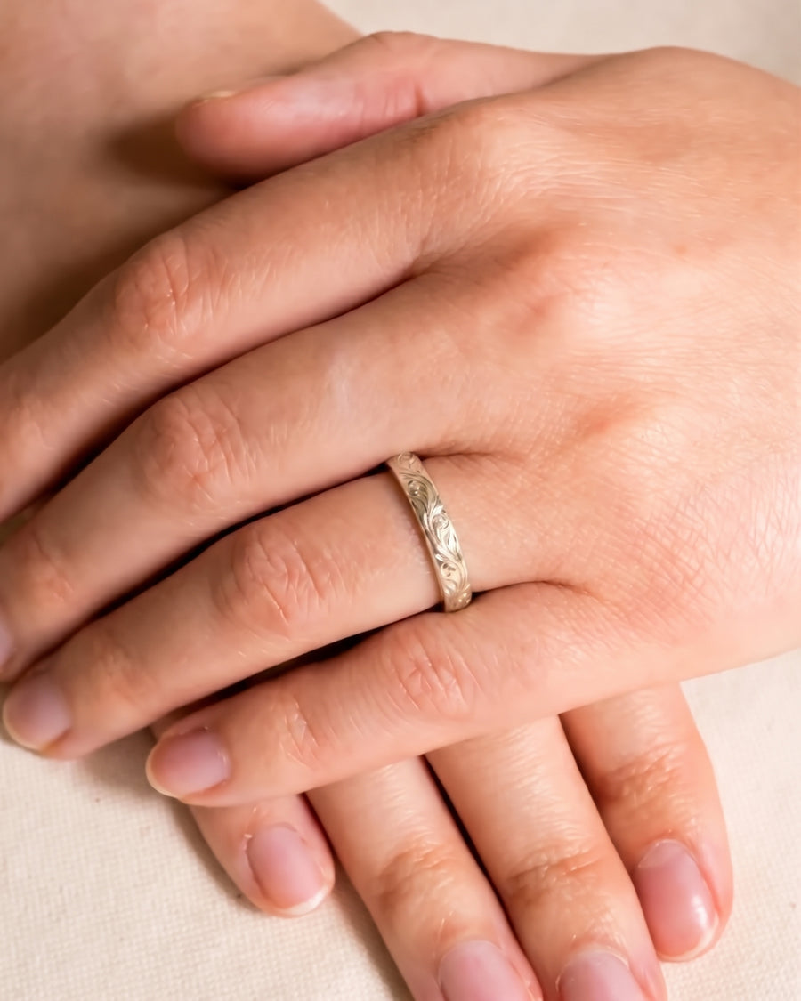 Silver wedding ring with intricate floral engravings worn on a finger.