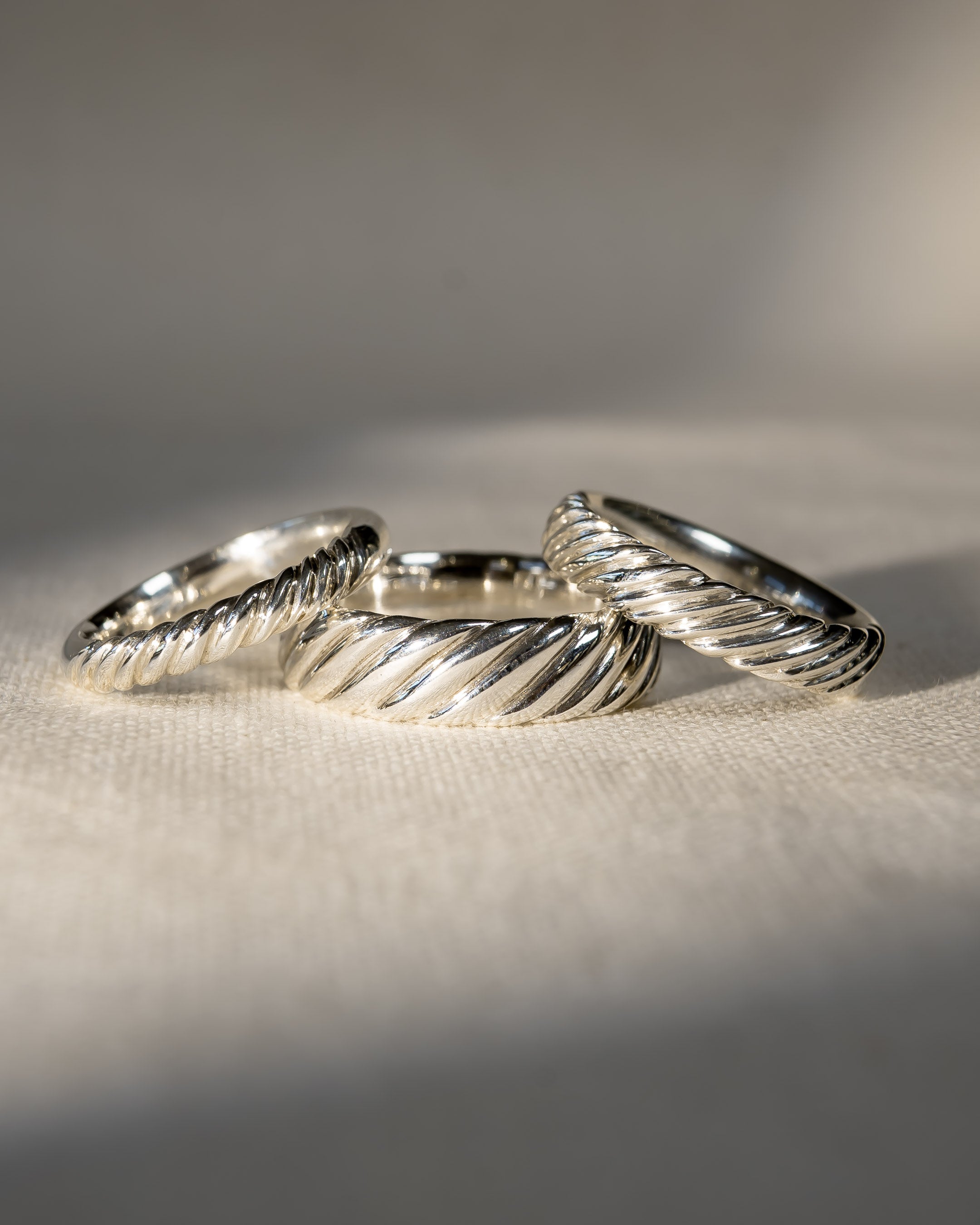 Three twisted silver wedding rings on a textured cream fabric in natural light