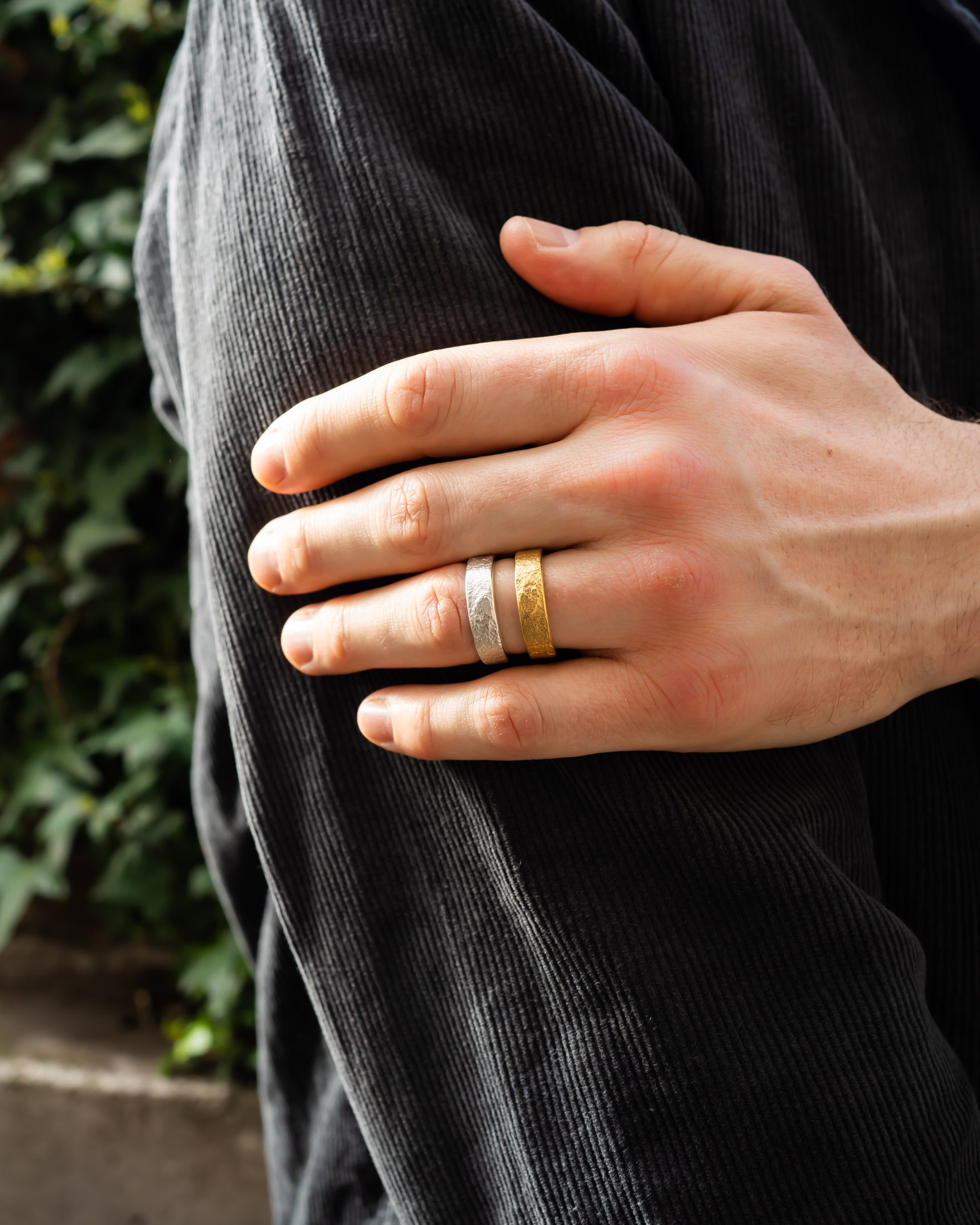 Hand wearing textured gold and silver wedding rings outdoors on a black jacket