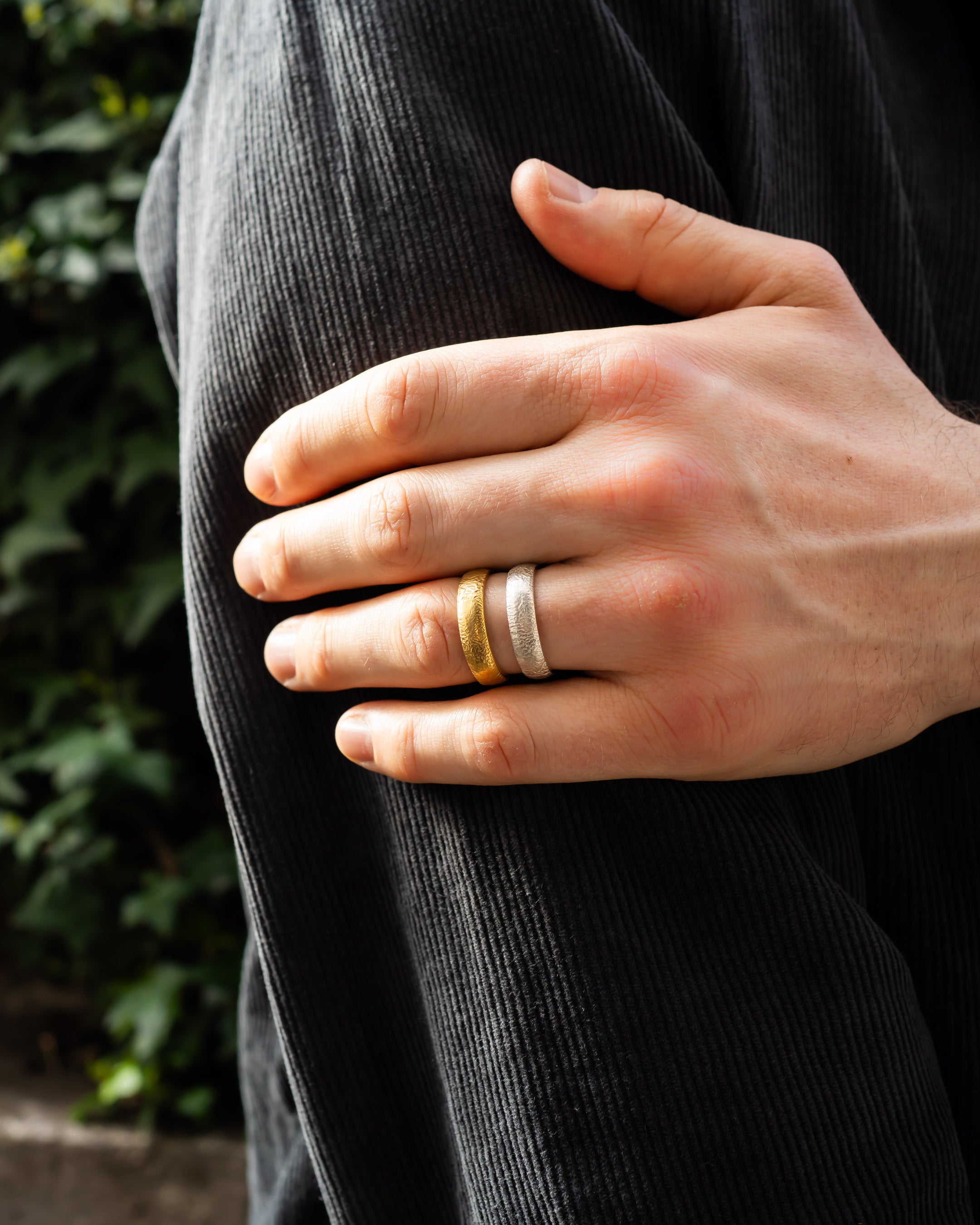 Hand wearing textured gold and silver wedding rings against dark fabric outdoors