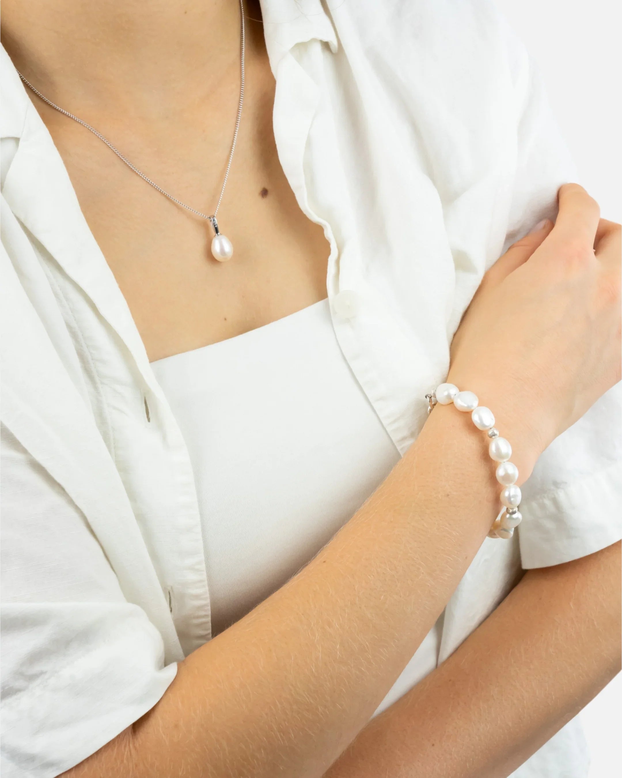 Woman wearing pearl necklace and pearl bracelet, dressed in a white shirt