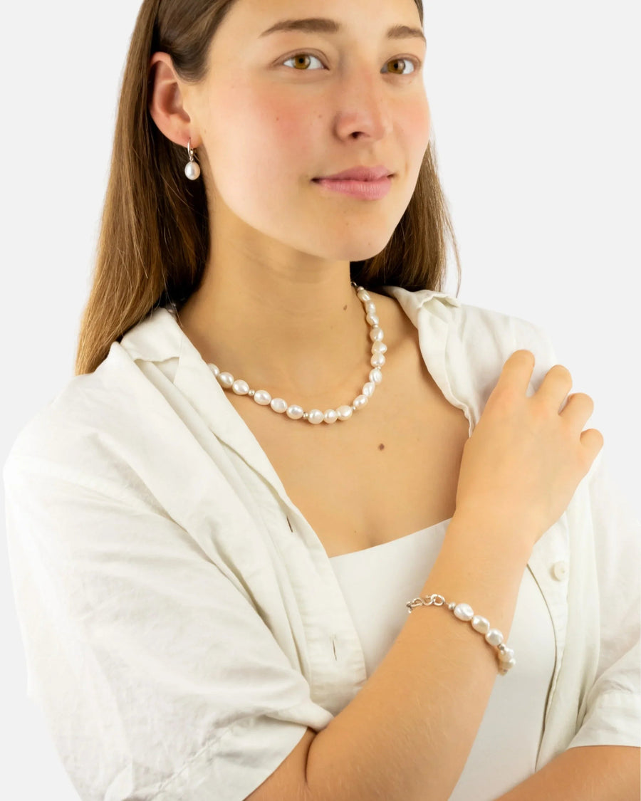 Woman wearing a pearl necklace, bracelet, and earrings with a white shirt