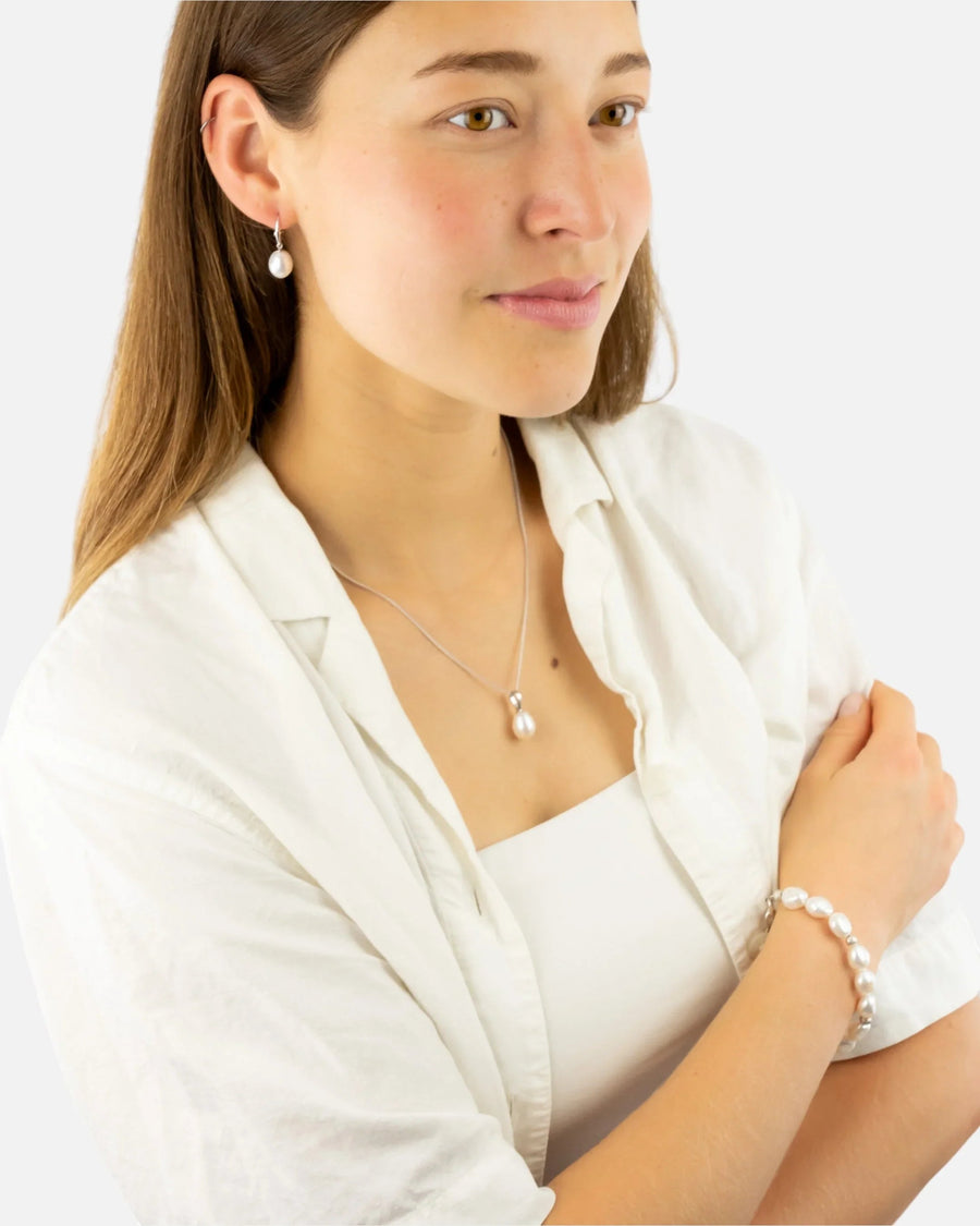 Woman wearing pearl drop earrings, necklace, and bracelet with silver accents
