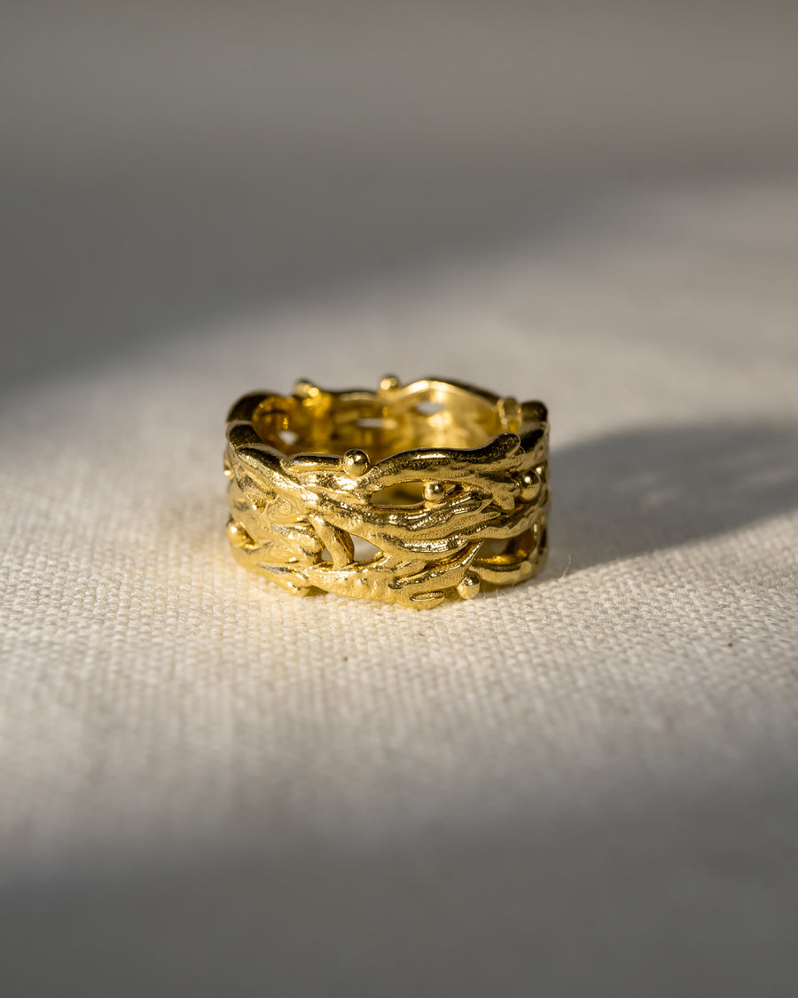Textured gold wedding ring with organic, intertwined design on a fabric background