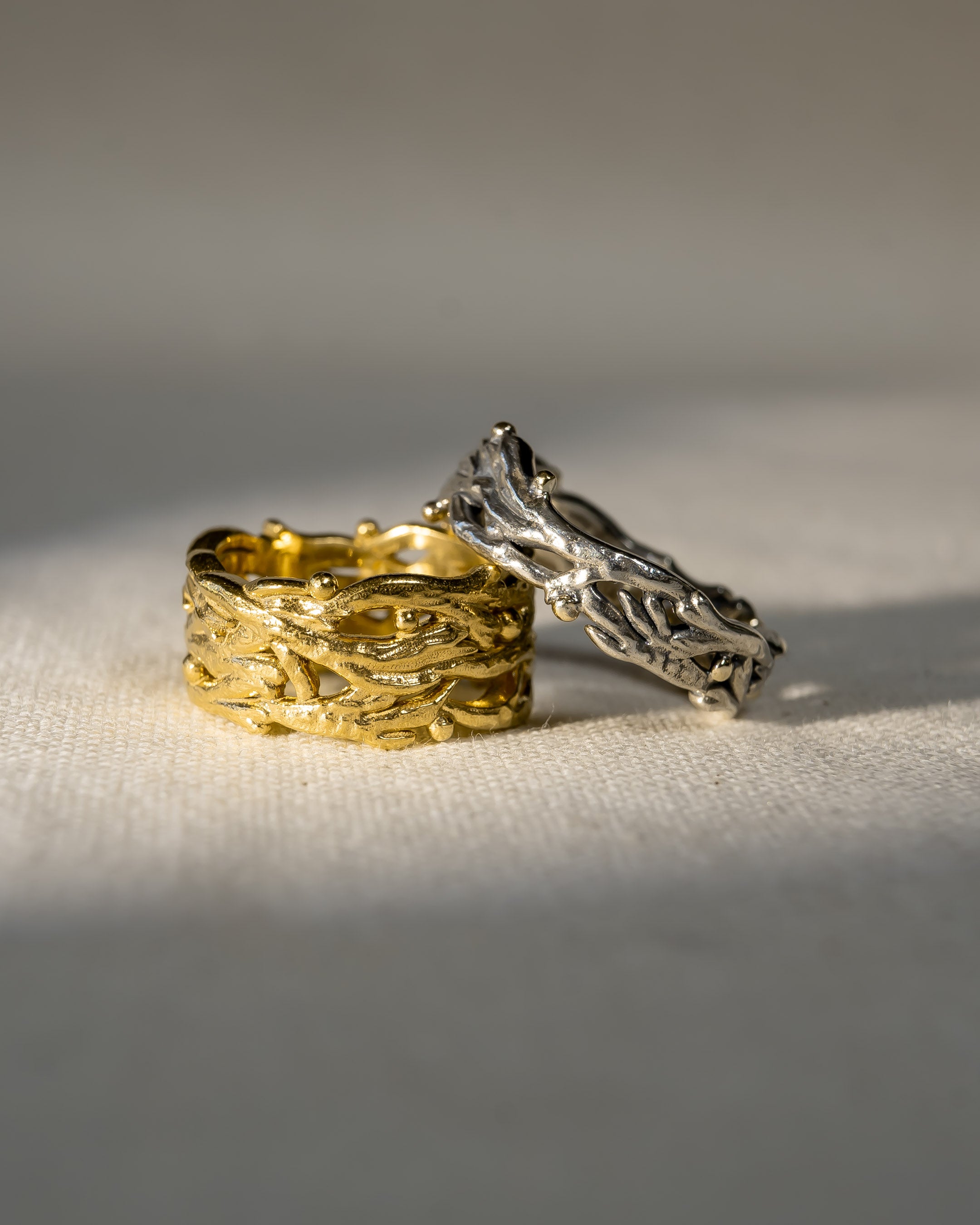 Gold and silver wedding rings with organic, nature-inspired textures on cream fabric