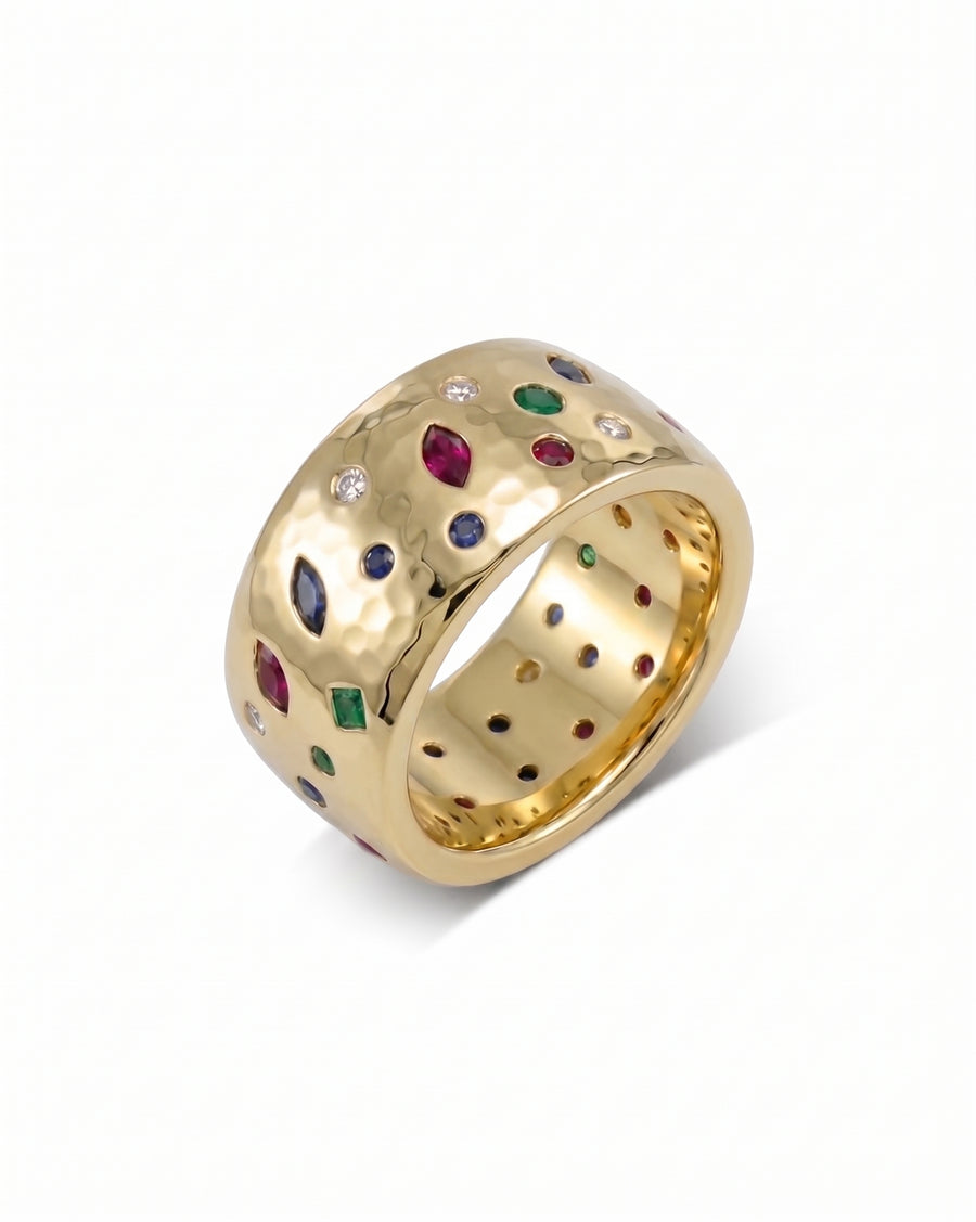 Wide hammered gold ring with scattered sapphire, emerald, ruby, and diamond gemstones.