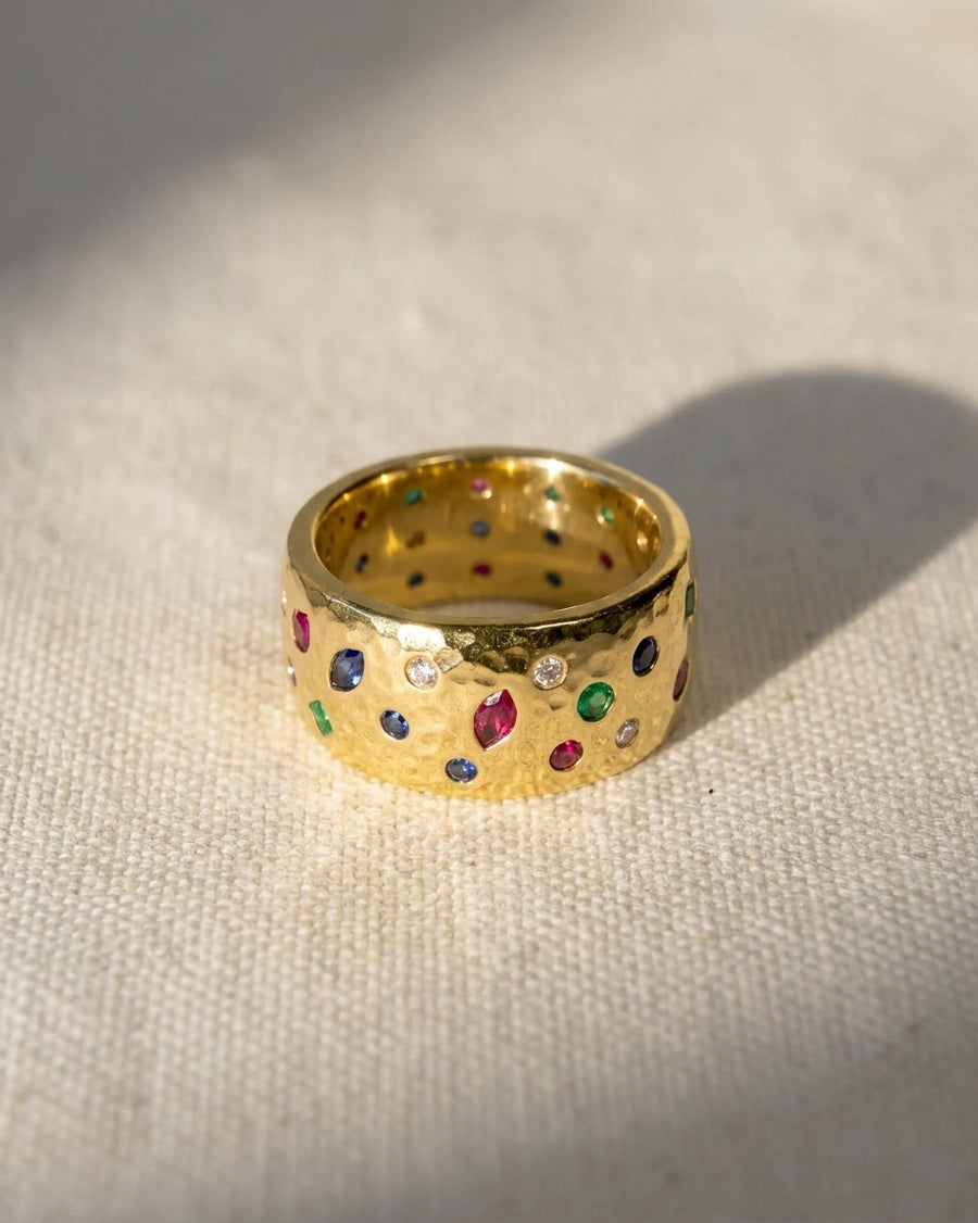 Wide 18ct yellow gold hammered ring with scattered sapphire, emerald, ruby, and diamond gemstones.