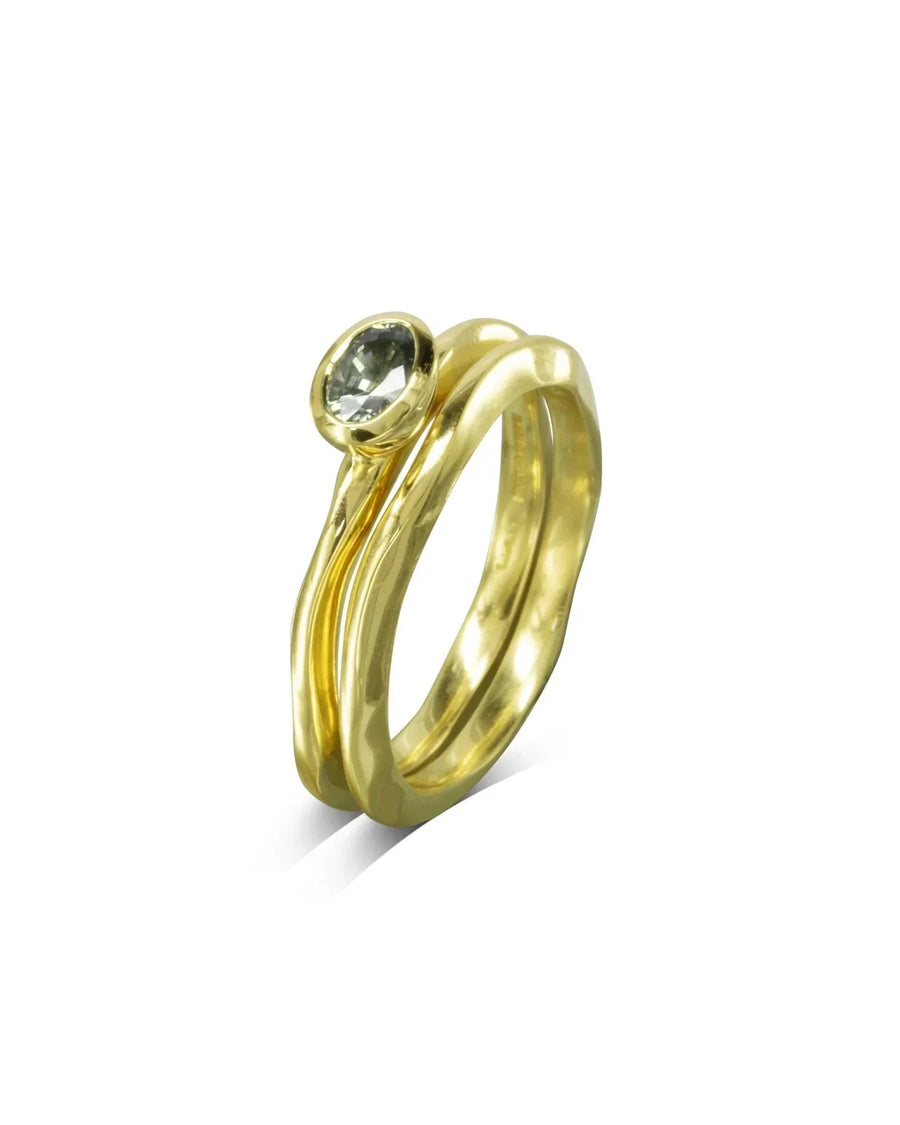 Gold dainty uneven wedding ring with a round green gemstone.