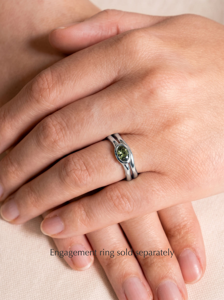 Silver wedding ring with an oval green gemstone on a finger, featuring a dainty, uneven band design.