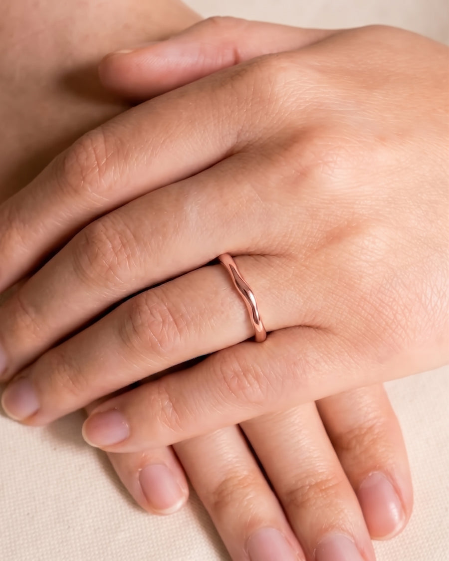 Dainty rose gold wedding ring with an uneven, wavy band worn on a woman's finger.