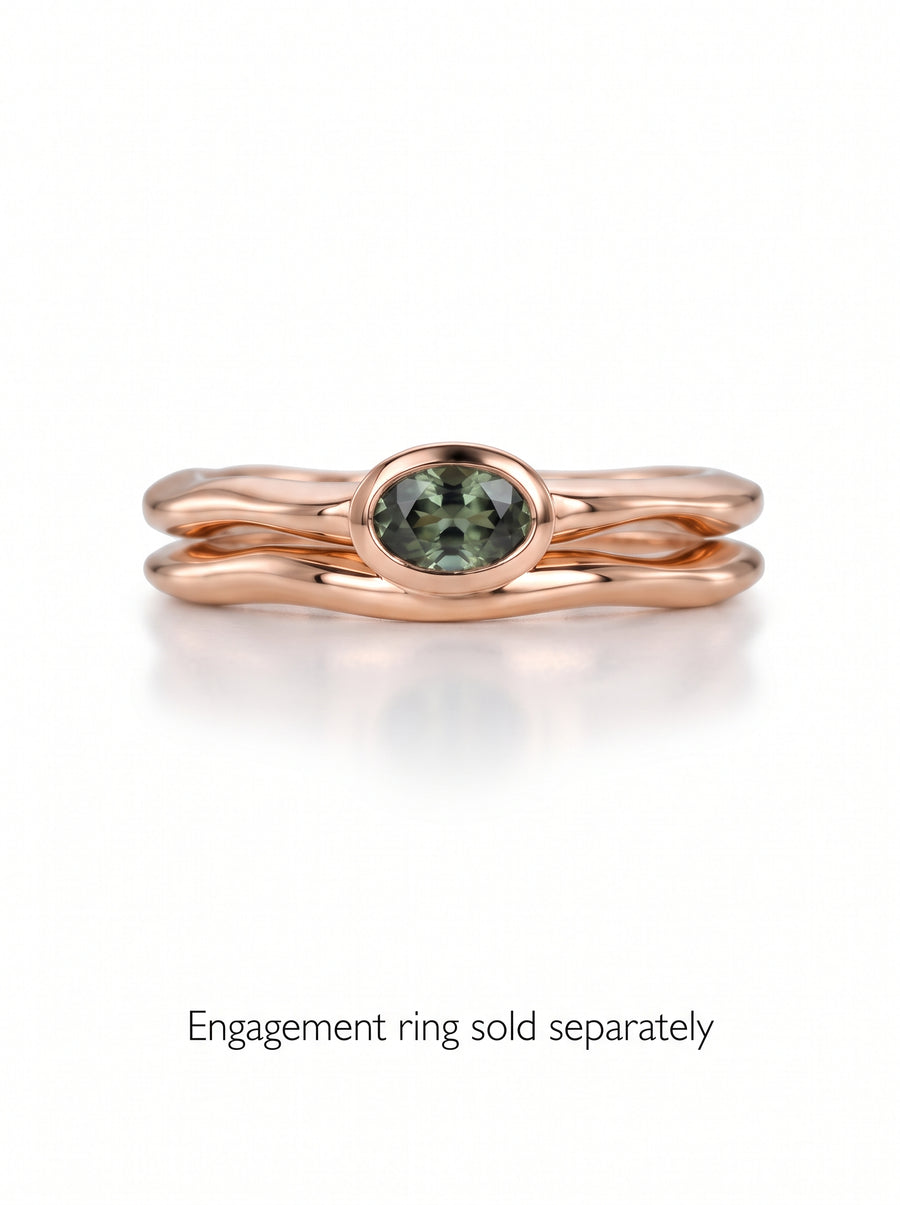 Rose gold wedding ring with an uneven, wavy band and a bezel-set oval green gemstone.