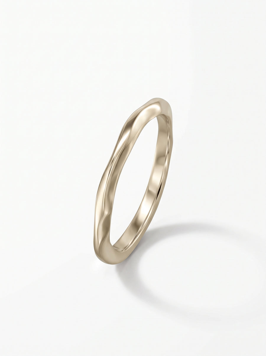 Dainty gold wedding ring with a smooth, uneven wavy band design on a white background.