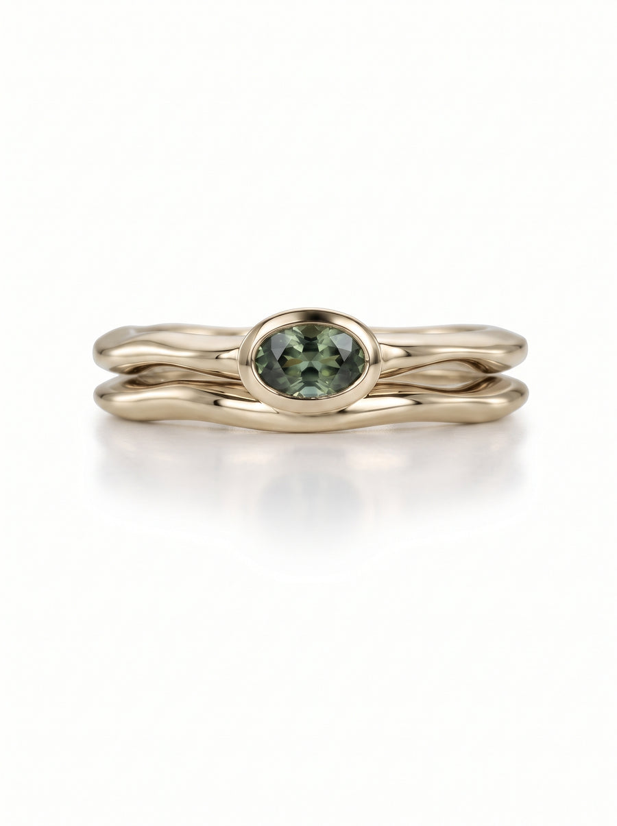 Dainty gold wedding ring set featuring an oval green gemstone in a smooth, uneven wavy band design.
