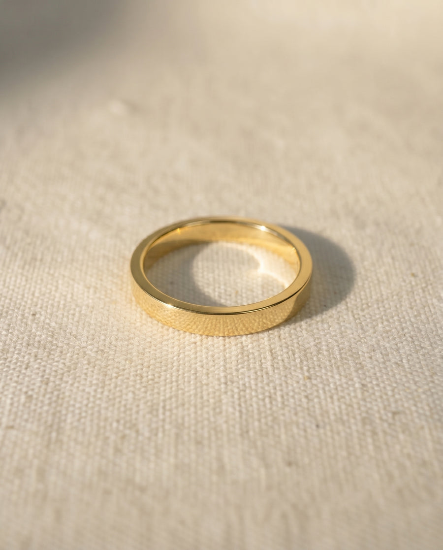 Gold flat wedding ring on a light fabric surface.