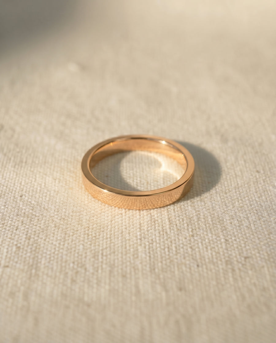 Rose gold flat wedding band on a cream fabric surface.