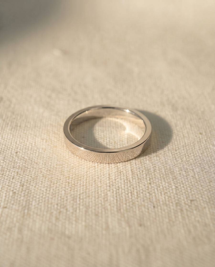 Silver flat wedding band on a light fabric surface.