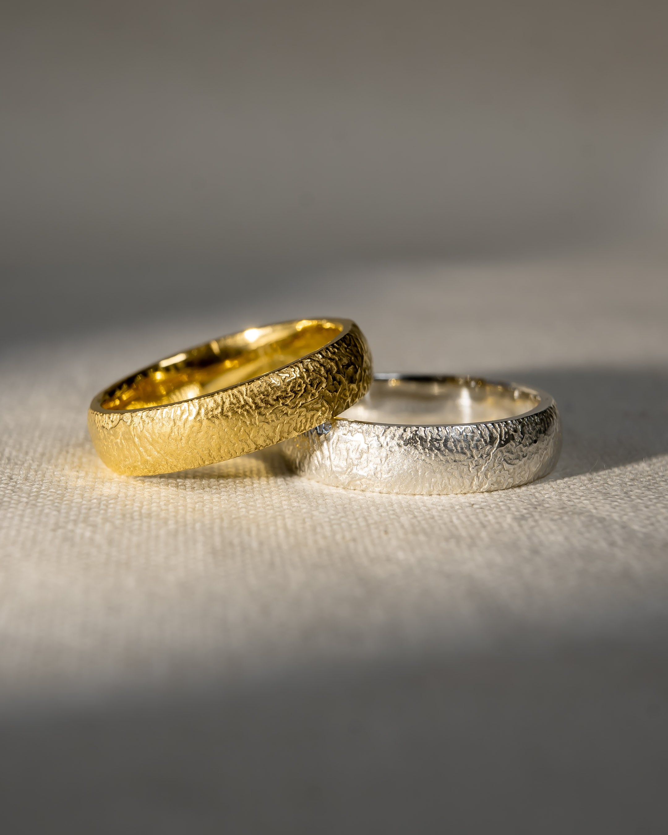 Textured gold and silver wedding rings on a neutral fabric background