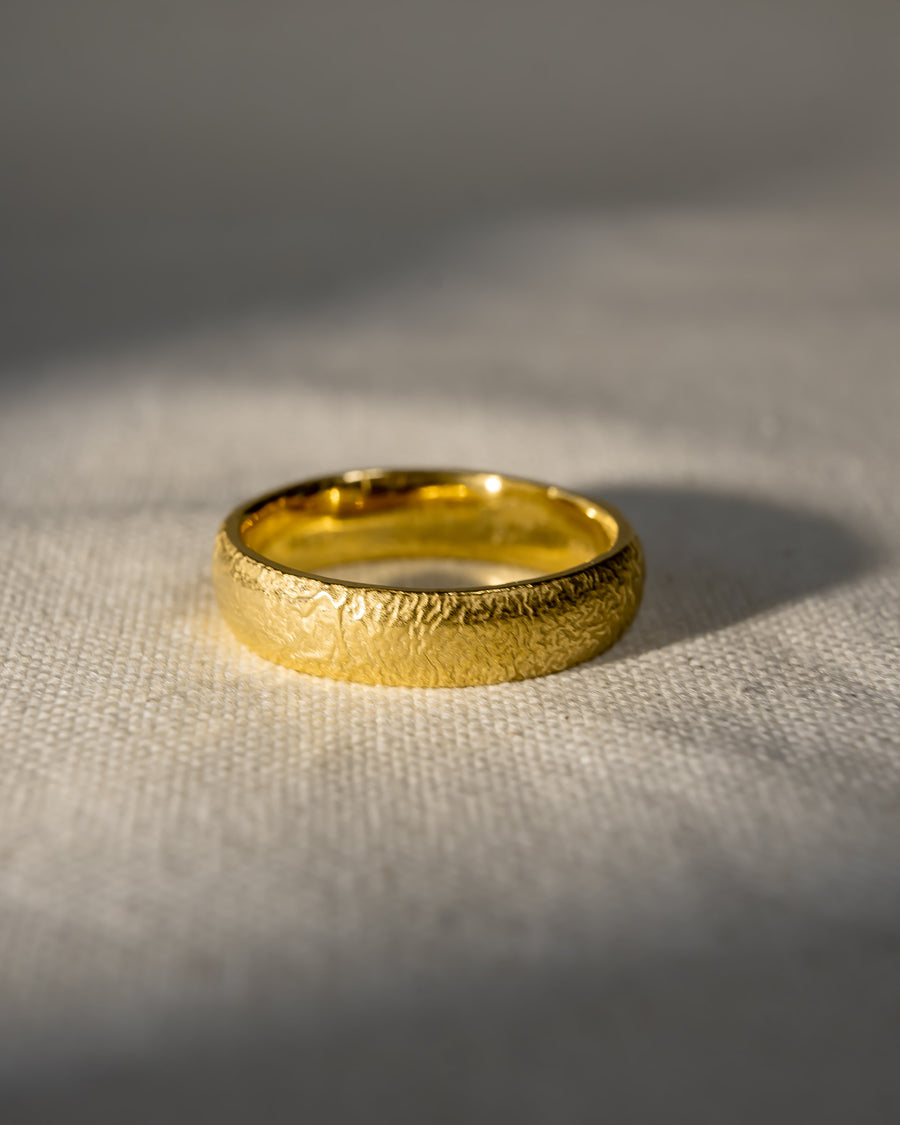 textured gold wedding band with organic design on neutral fabric background