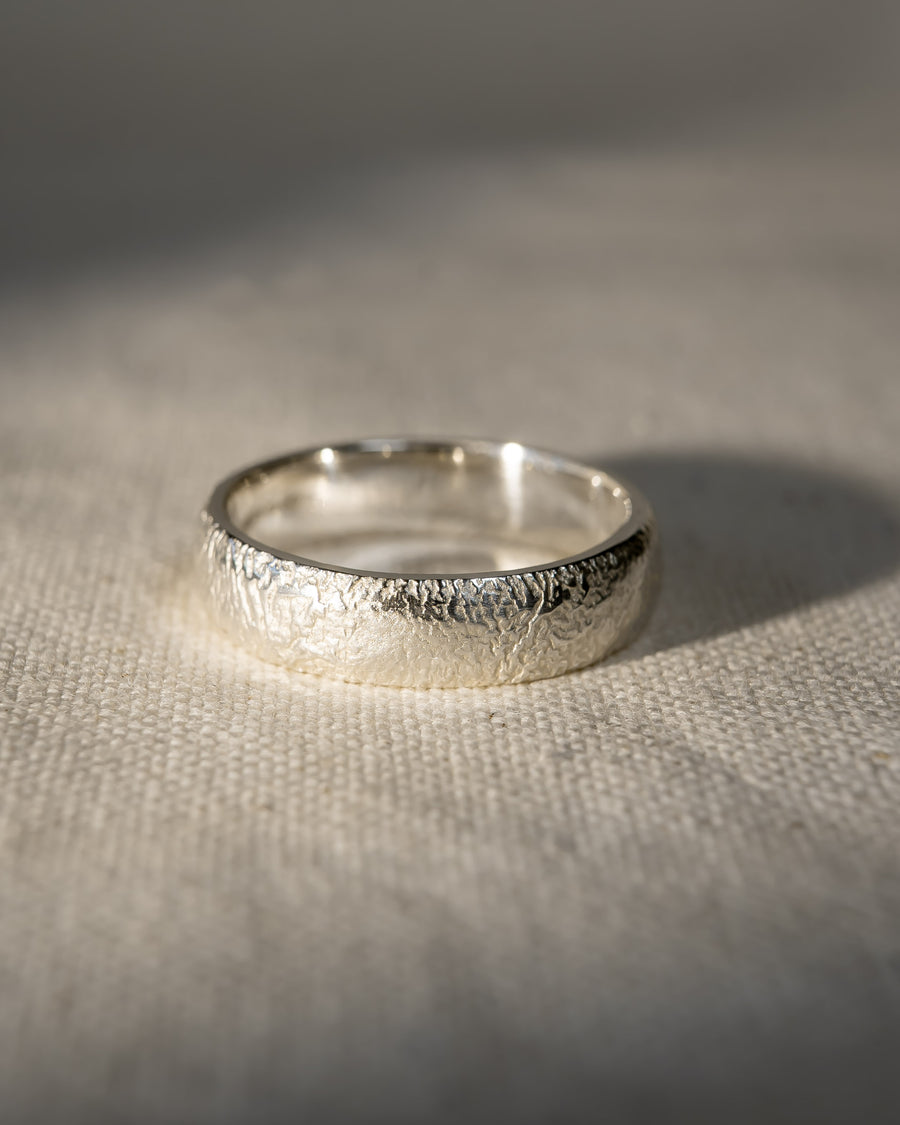 Textured silver wedding ring with organic finish on a light fabric surface