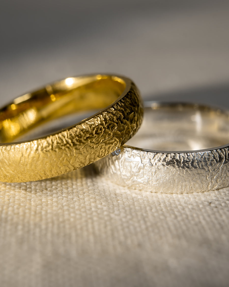 Textured gold and silver wedding rings with organic, handcrafted finish on fabric background