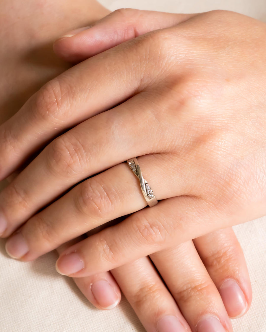 Silver wedding ring with a twisted design and small diamonds on a woman's hand.