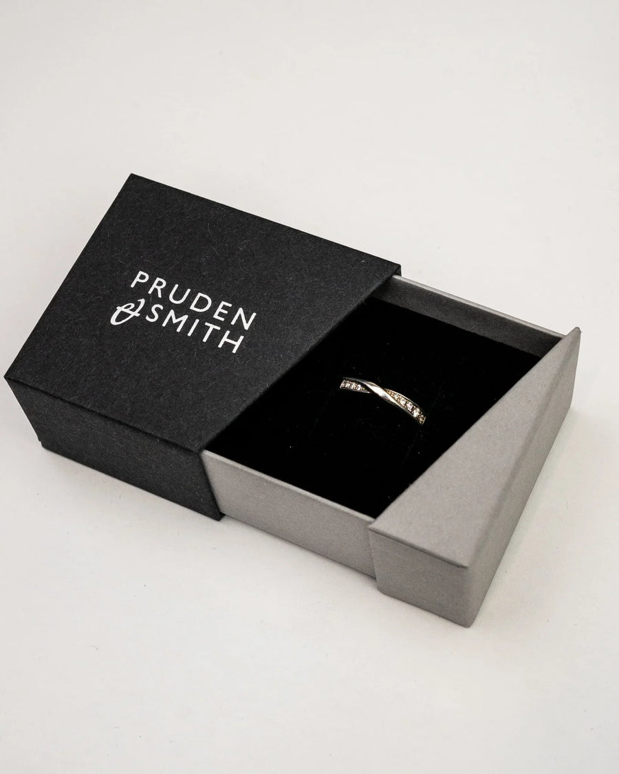 Silver wedding ring with a twisted band and small diamonds, presented in an open black box.