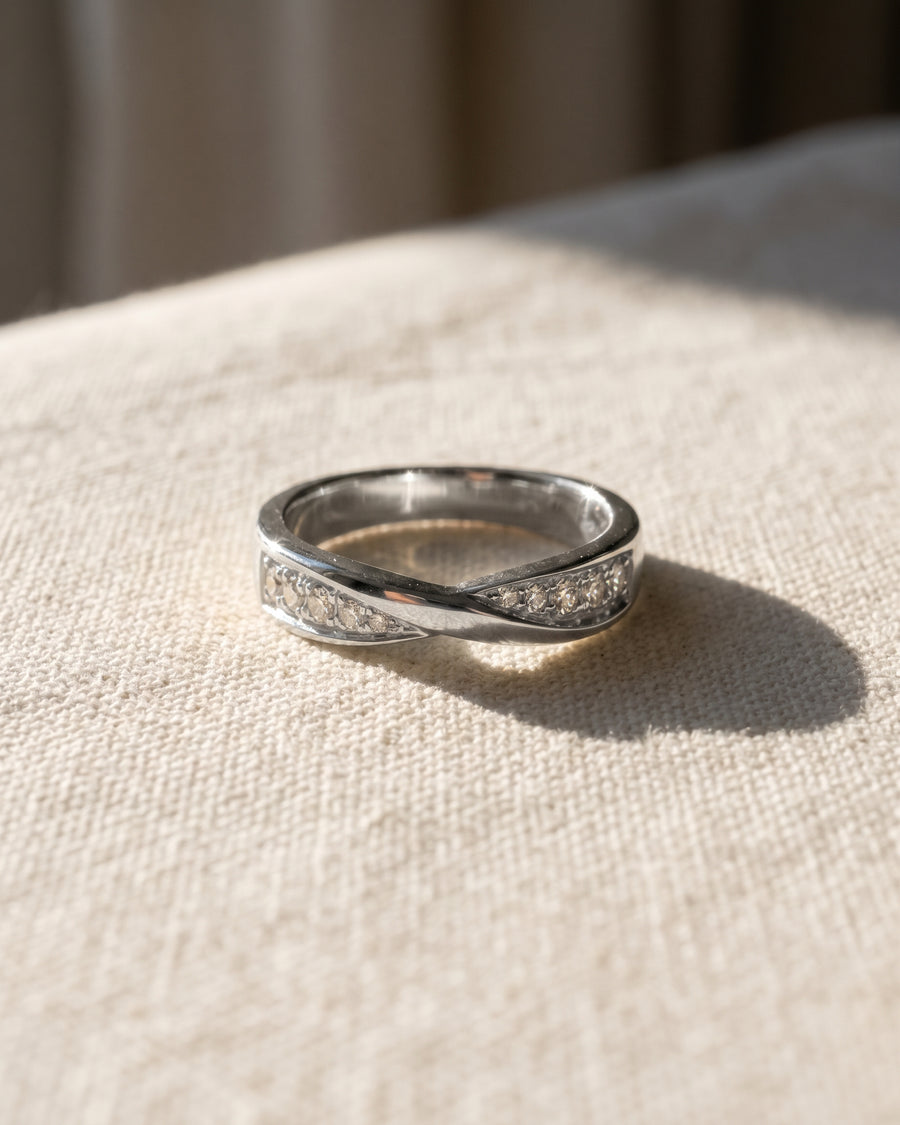 Silver wedding ring with a twisted band design and small embedded diamonds on a textured fabric surface.