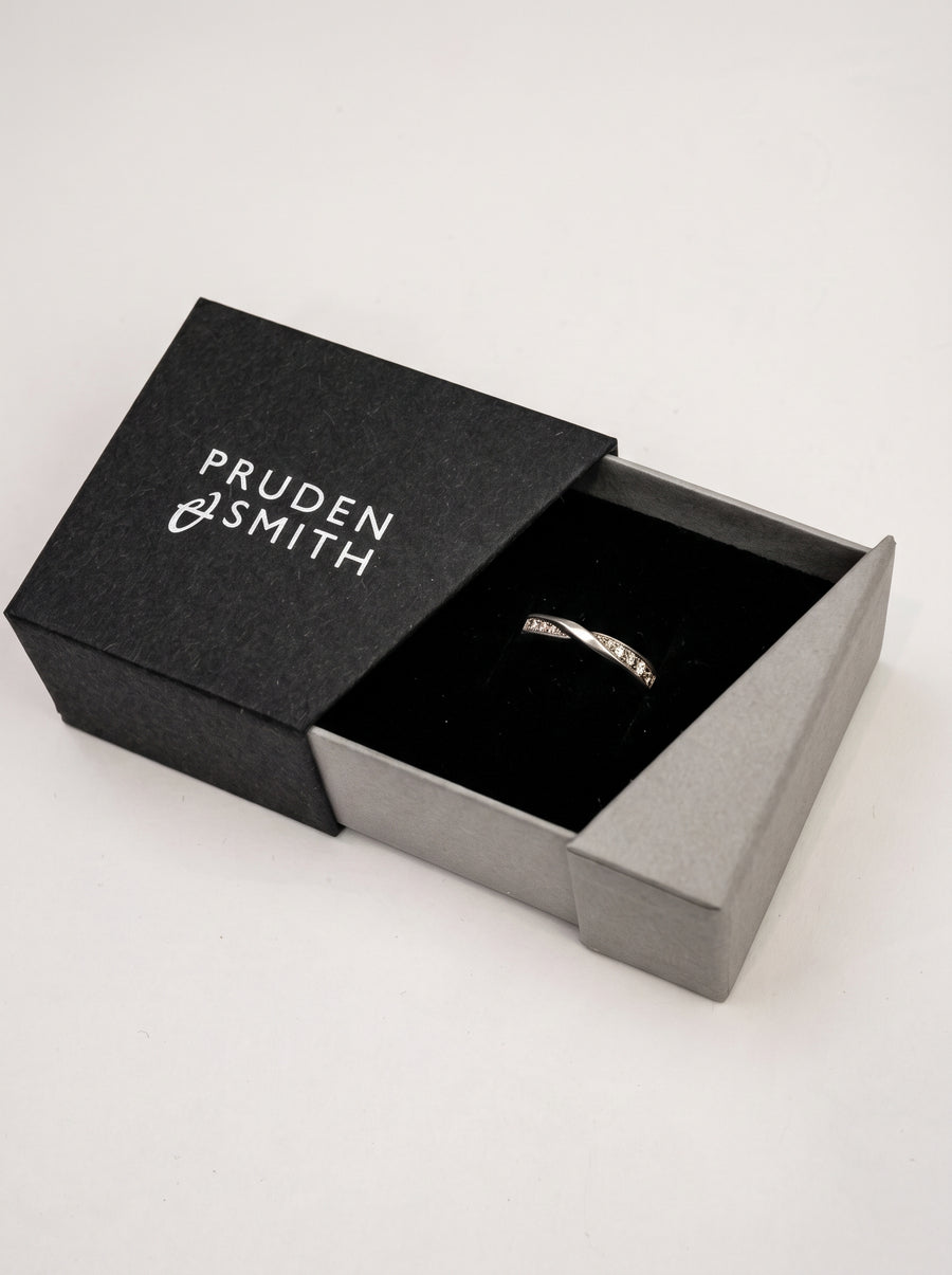 Silver wedding ring with a twisted band and small embedded diamonds inside a black jewelry box.