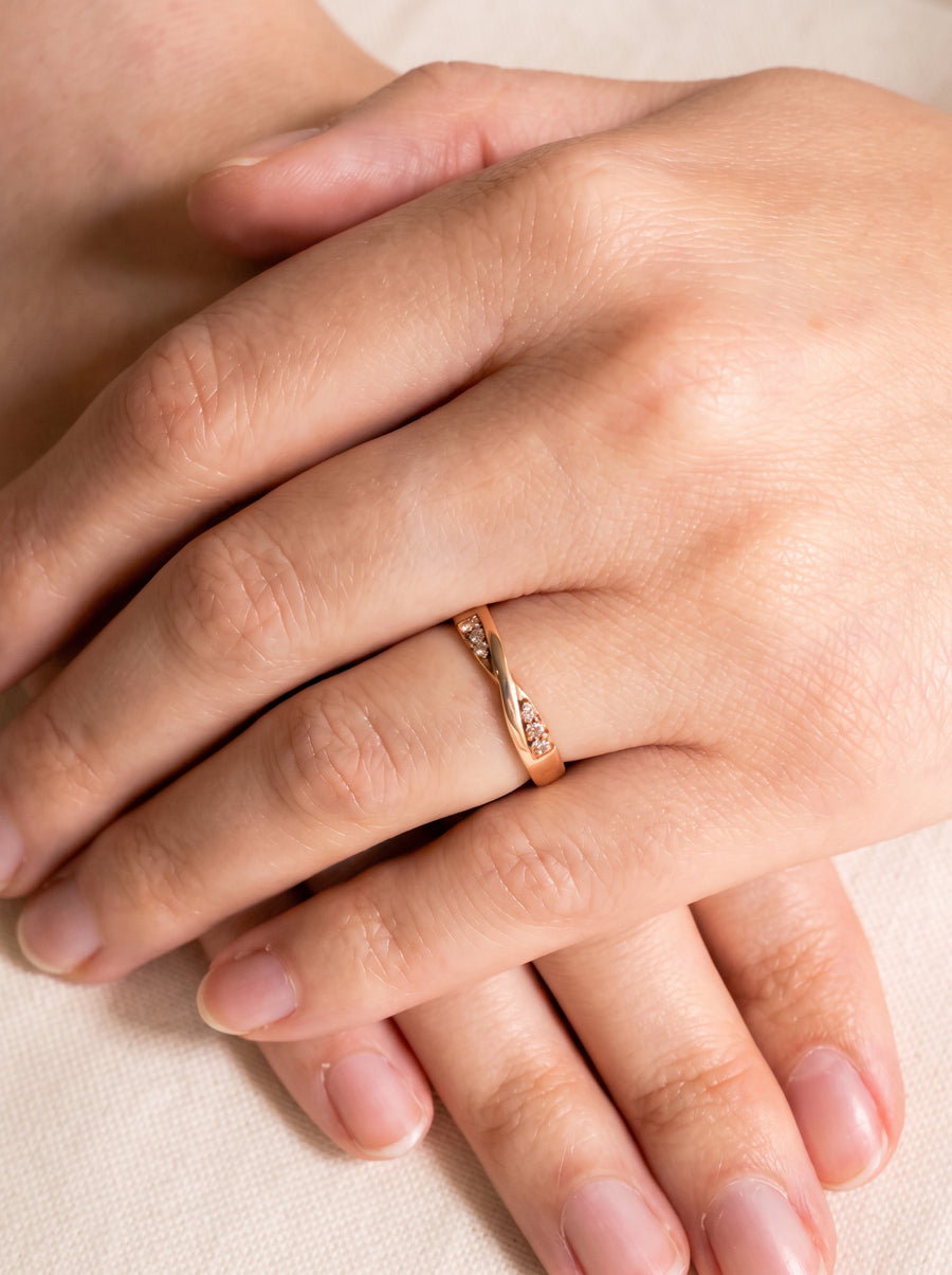 Rose gold wedding ring with a twisted band design and small embedded diamonds worn on a finger.