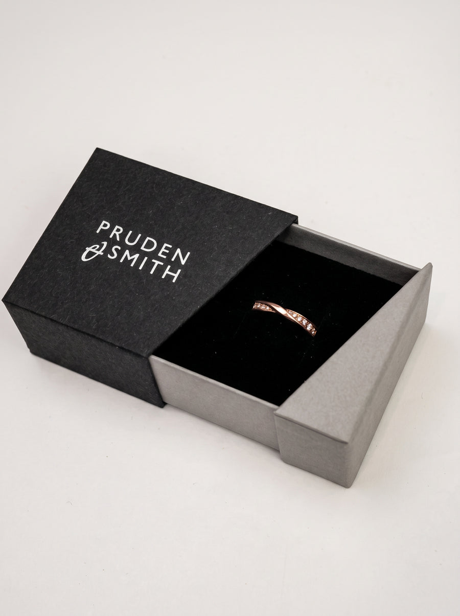 Rose gold wedding ring with a twisted band and small inset diamonds in a black jewelry box.