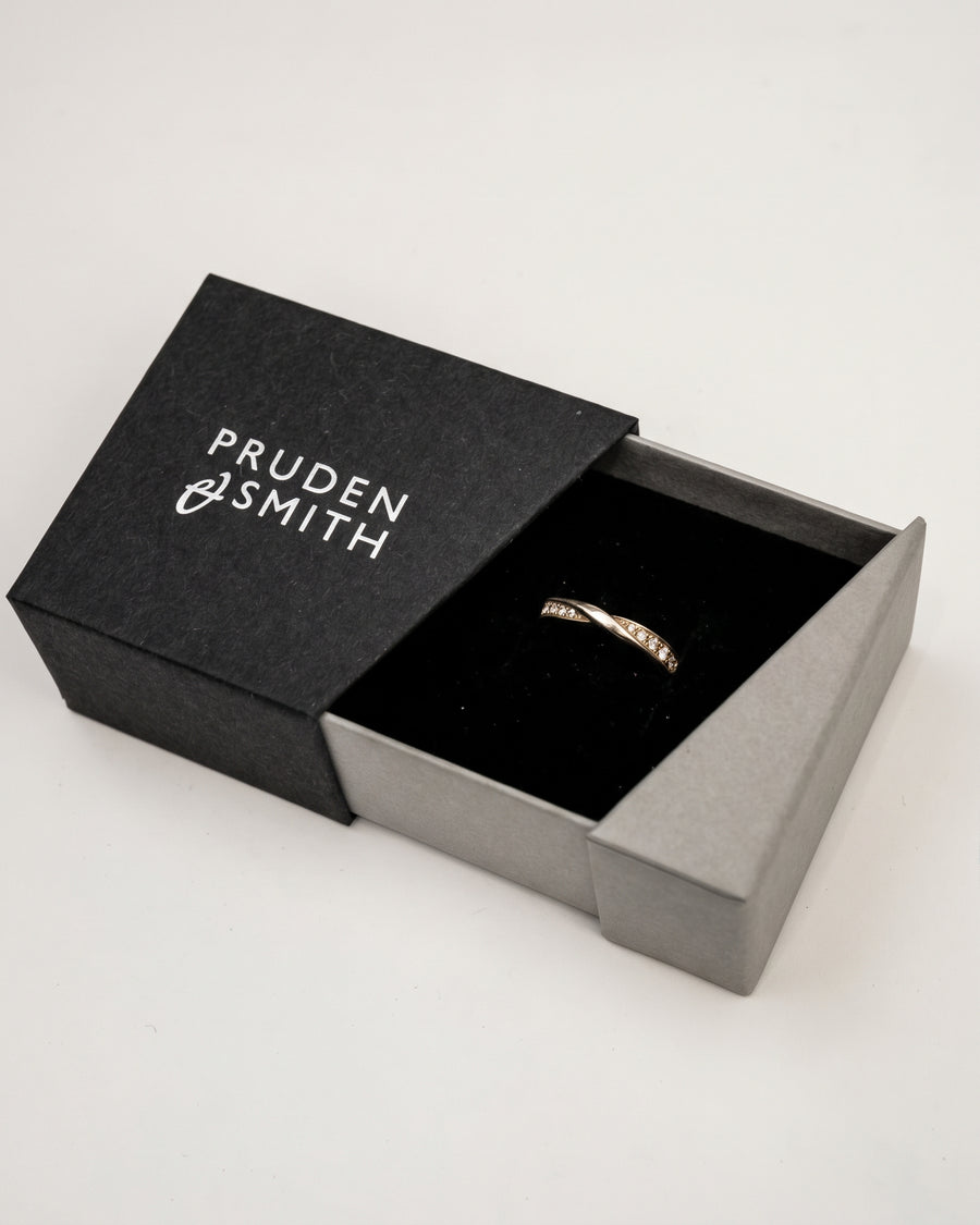Gold wedding ring with a twisted design and small diamonds in a black jewelry box.