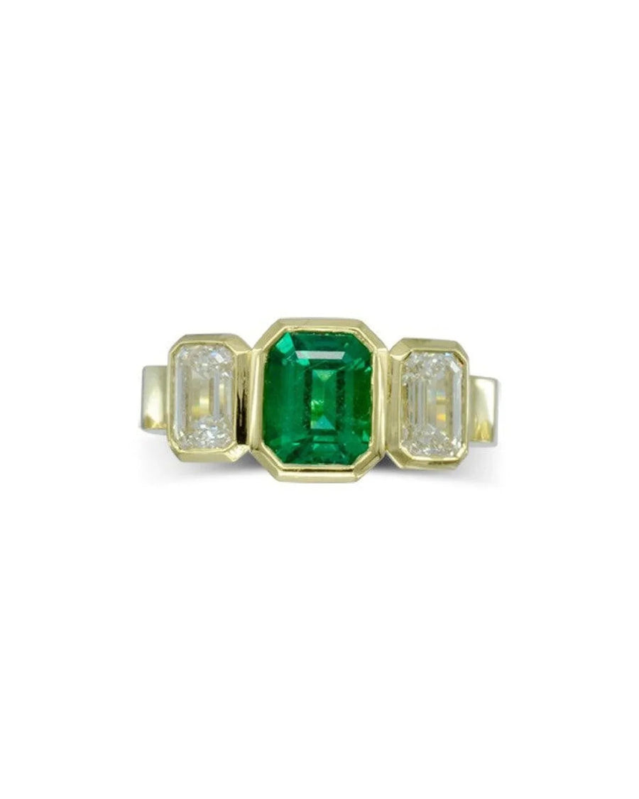 Yellow gold trilogy ring with a central emerald and two side diamonds.